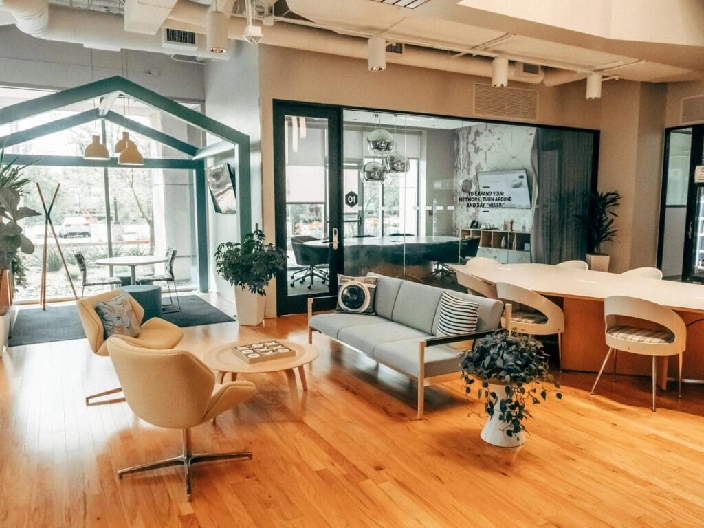 Un espace de coworking bien conçu avec des sièges confortables, une table de réunion et un espace de travail privatif en forme de maison. L'espace comprend des meubles modernes, un sol en bois et une salle de réunion vitrée.